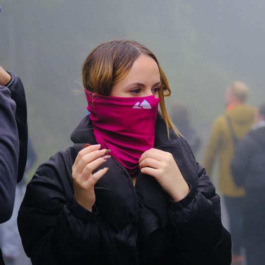 Neck buff gaiter displayed in a female model. With a white mountain logo. Burgundy colour. 